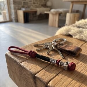 Dragonne en paracorde bordeaux et noire posée sur une table en bois avec un trousseau de clés Dragonne en paracorde bordeaux et noire posée sur une table en bois avec un trousseau de clés