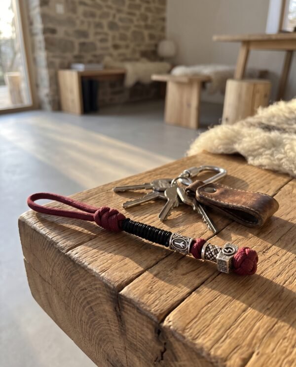Dragonne en paracorde bordeaux et noire posée sur une table en bois avec un trousseau de clés Dragonne en paracorde bordeaux et noire posée sur une table en bois avec un trousseau de clés
